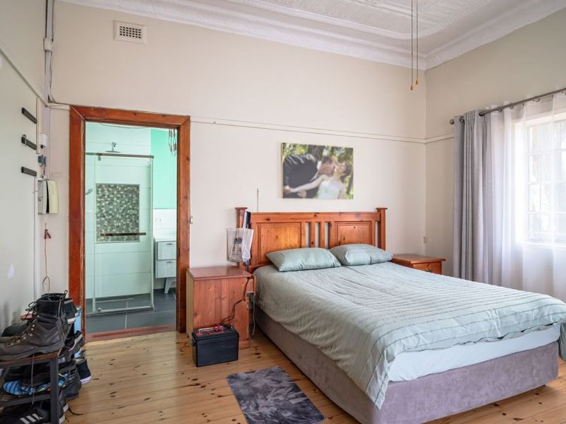 A bedroom featuring original timber flooring, ornate ceiling details, and an adjoining en-suite bathroom with a glass-enclosed shower.