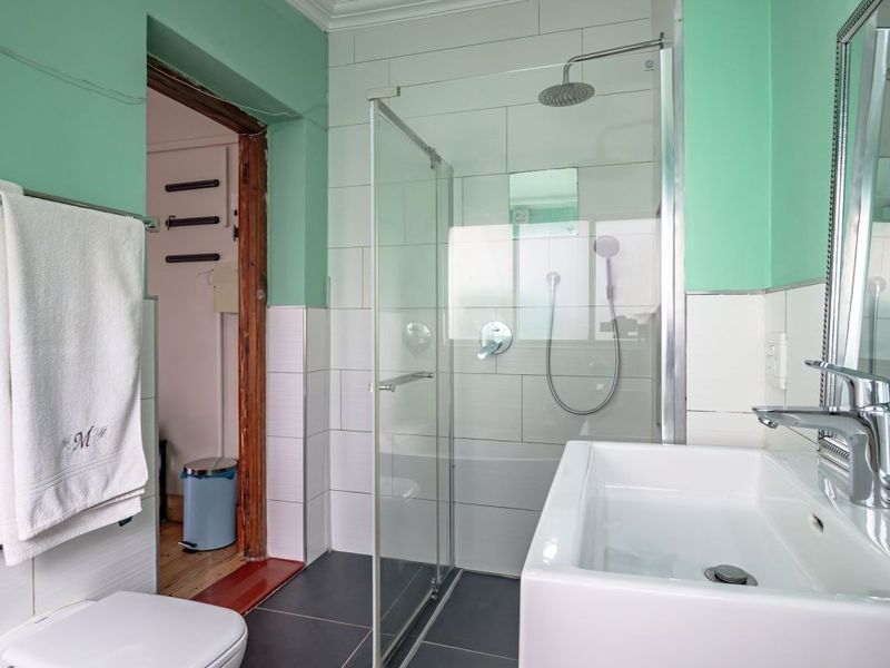 A functional bathroom featuring a walk-in shower with glass screen, modern basin, and tiled finishes. The space is well-lit and clean.