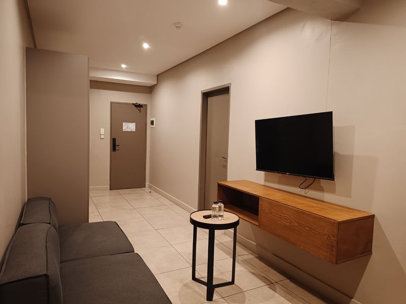 A modern living area featuring neutral wall tones, tiled flooring, recessed lighting, and a sleek wall-mounted media console.