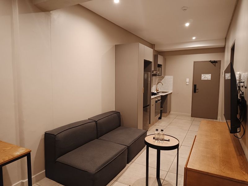 Compact open-plan apartment living area featuring a kitchenette with built-in cabinetry, tiled flooring, and recessed lighting.