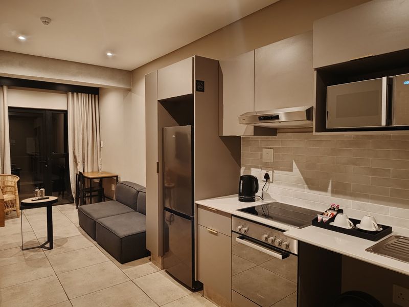 Modern open-plan apartment featuring a compact kitchen with built-in appliances, subway tile backsplash, and tiled flooring, seamlessly flowing into the living area.