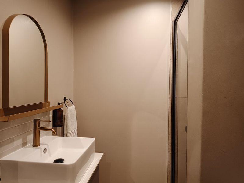 A modern bathroom featuring a vessel sink with a brass faucet, an arched mirror, and a glass-enclosed shower.