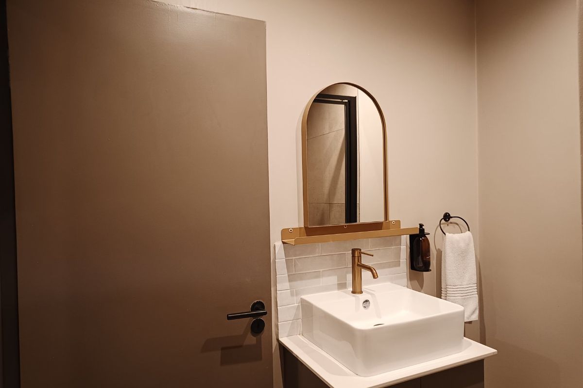 A modern bathroom vanity featuring a white vessel sink, brass faucet, subway tile backsplash, and an arched mirror.
