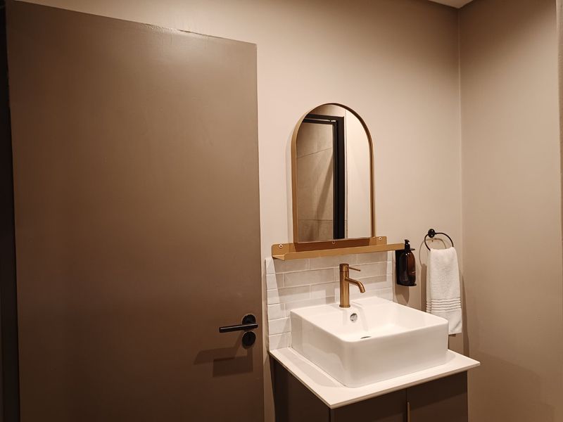 A modern bathroom vanity featuring a white vessel sink, brass faucet, subway tile backsplash, and an arched mirror.