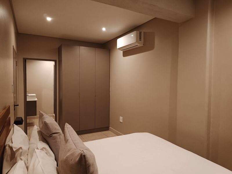A well-maintained bedroom featuring a built-in wardrobe, split-system air conditioning, and recessed lighting, with an adjoining en-suite bathroom visible.