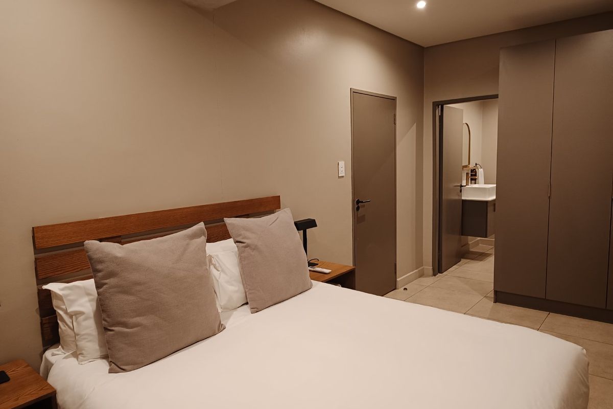 A well-maintained bedroom featuring neutral tones, tiled flooring, built-in cupboards, and direct access to an en-suite bathroom.