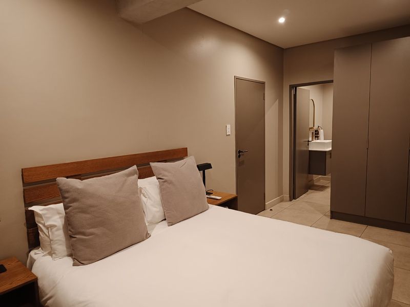 A well-maintained bedroom featuring neutral tones, tiled flooring, built-in cupboards, and direct access to an en-suite bathroom.