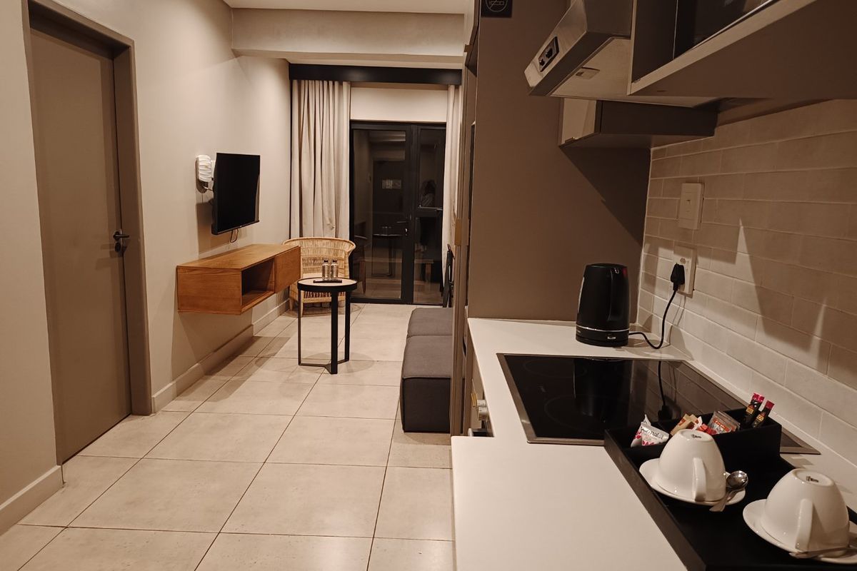 Modern open-plan apartment featuring a compact kitchen with built-in hob and extractor, flowing into a living area with tiled floors and balcony access.