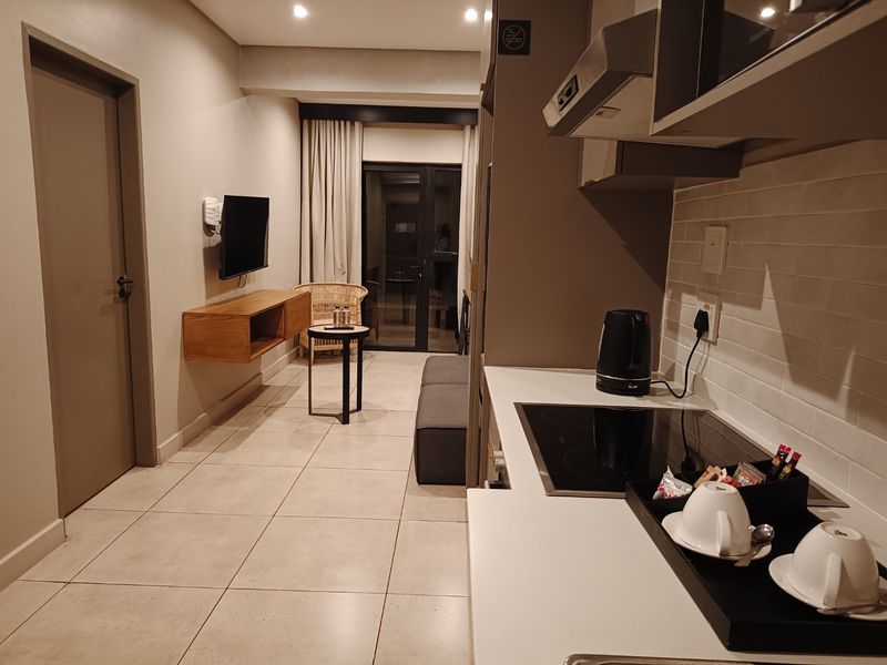 Modern open-plan apartment featuring a compact kitchen with built-in hob and extractor, flowing into a living area with tiled floors and balcony access.