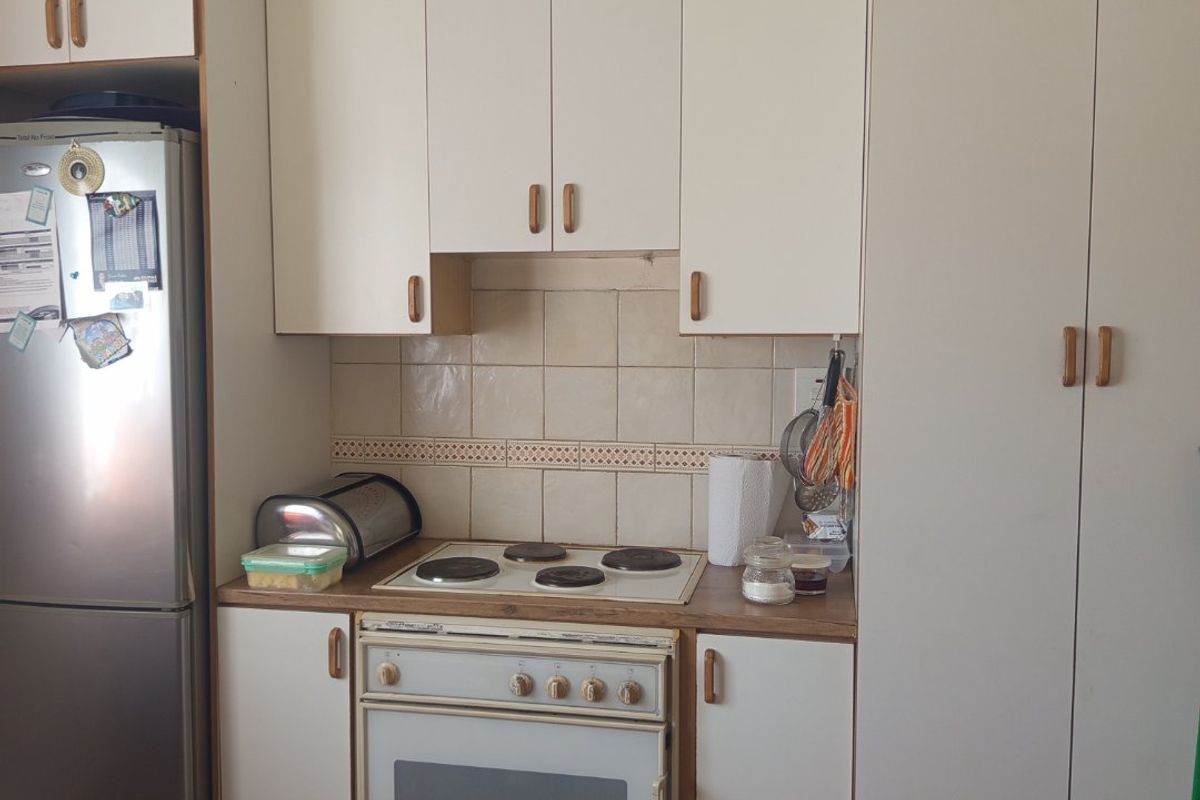 A compact kitchen featuring white built-in cabinetry, an electric cooktop, an oven, and a tiled backsplash with timber flooring.