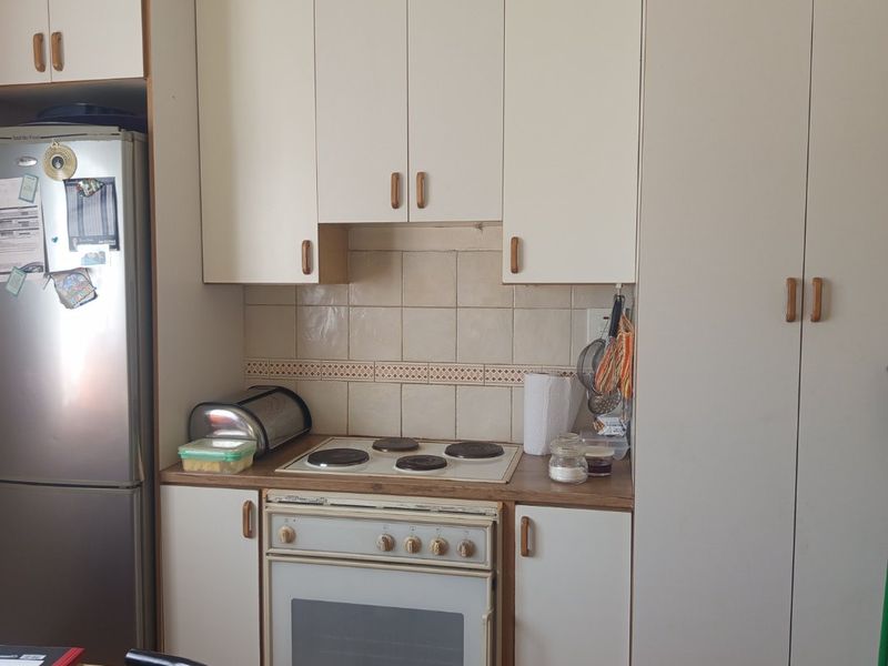A compact kitchen featuring white built-in cabinetry, an electric cooktop, an oven, and a tiled backsplash with timber flooring.