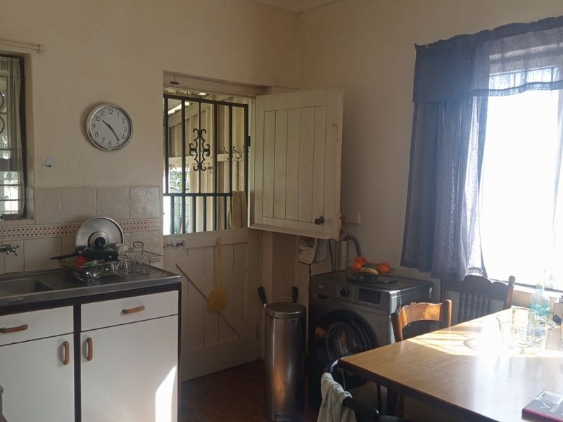 A functional kitchen area featuring timber flooring, built-in cabinetry, and a tiled splashback, with direct access to an exterior security door.