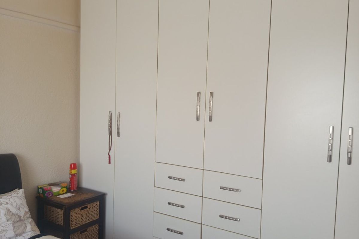 A bedroom featuring extensive white built-in cupboards with integrated drawers and warm timber flooring.