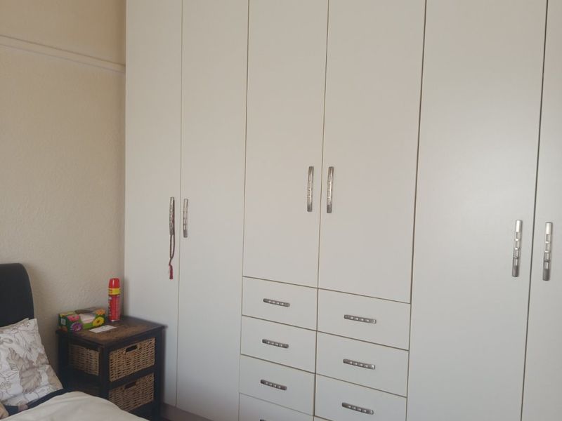 A bedroom featuring extensive white built-in cupboards with integrated drawers and warm timber flooring.