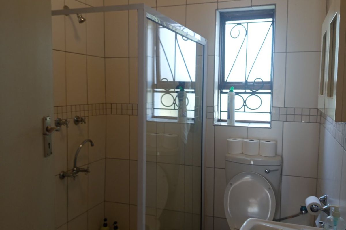 Compact bathroom featuring a shower enclosure, pedestal basin, and toilet with tiled finishes and security bars on the window.