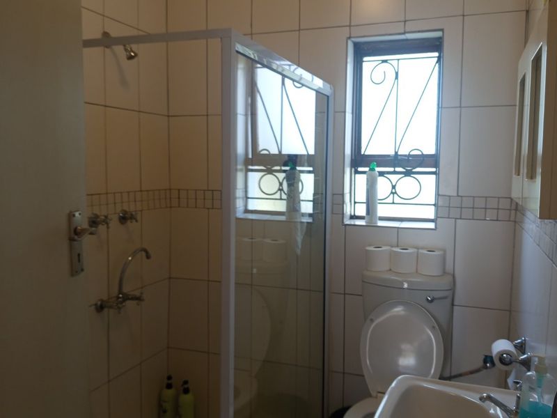 Compact bathroom featuring a shower enclosure, pedestal basin, and toilet with tiled finishes and security bars on the window.