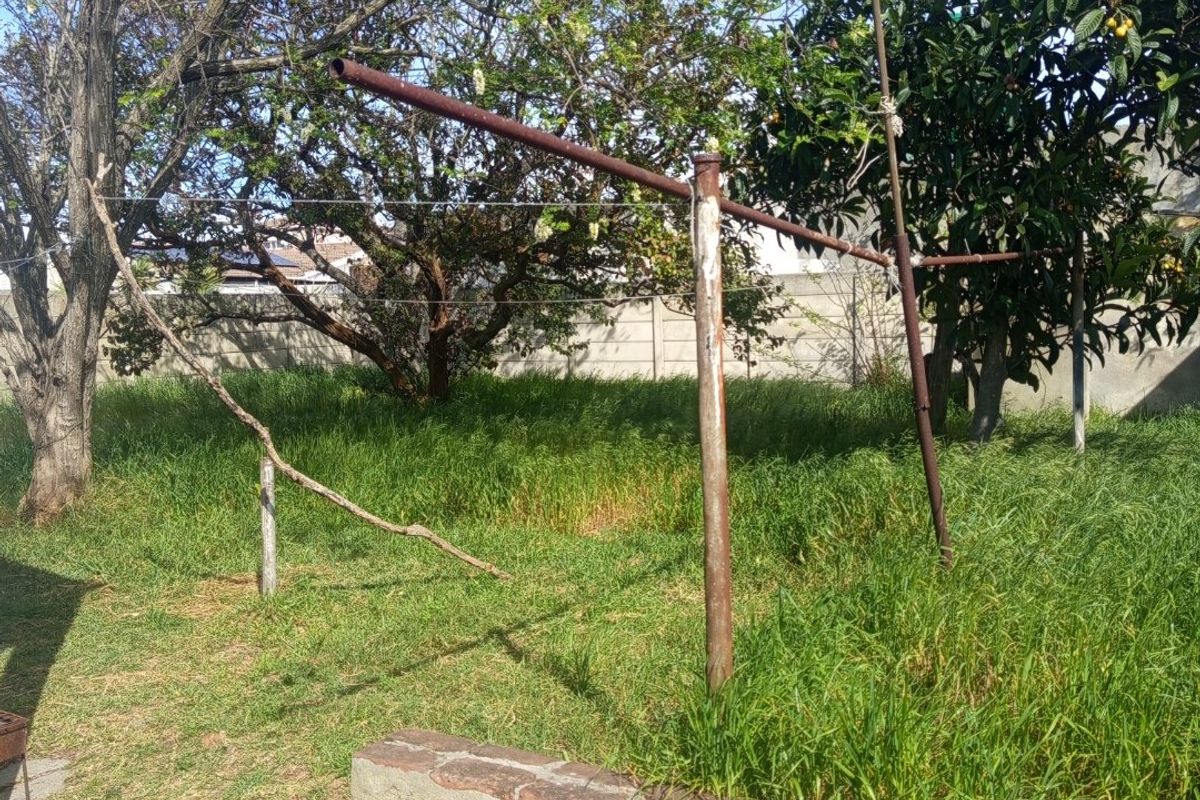 A large, overgrown garden area featuring a rusted metal washing line and a weathered brick retaining wall, offering significant potential for landscaping.