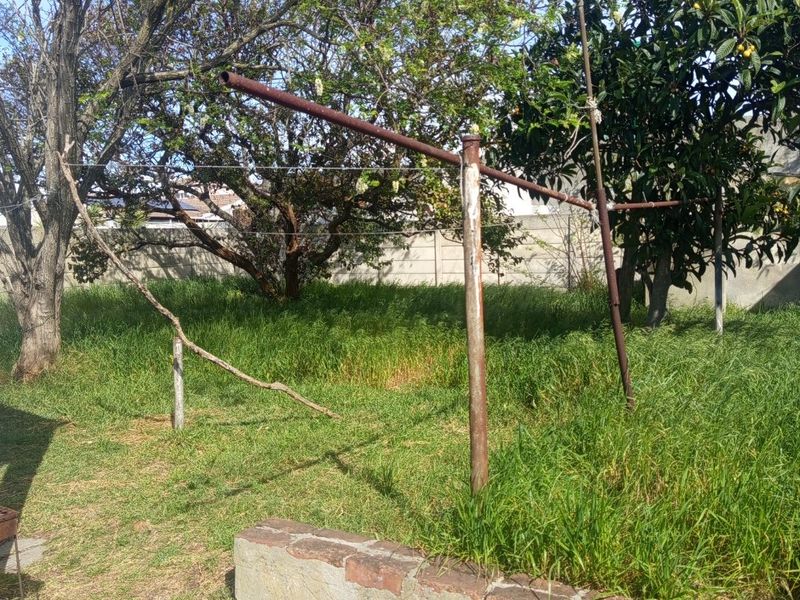A large, overgrown garden area featuring a rusted metal washing line and a weathered brick retaining wall, offering significant potential for landscaping.