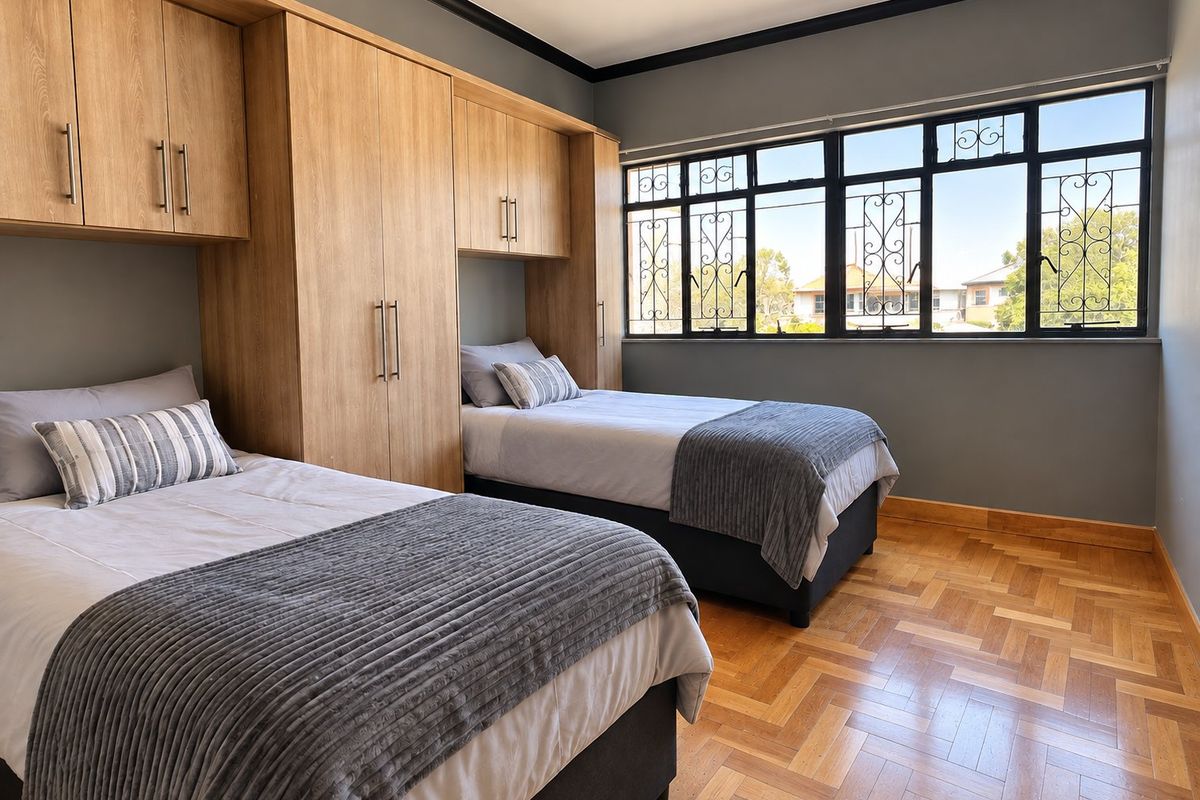 A well-maintained bedroom featuring warm parquet flooring, extensive built-in wooden cabinetry, and large steel-framed windows with security bars.