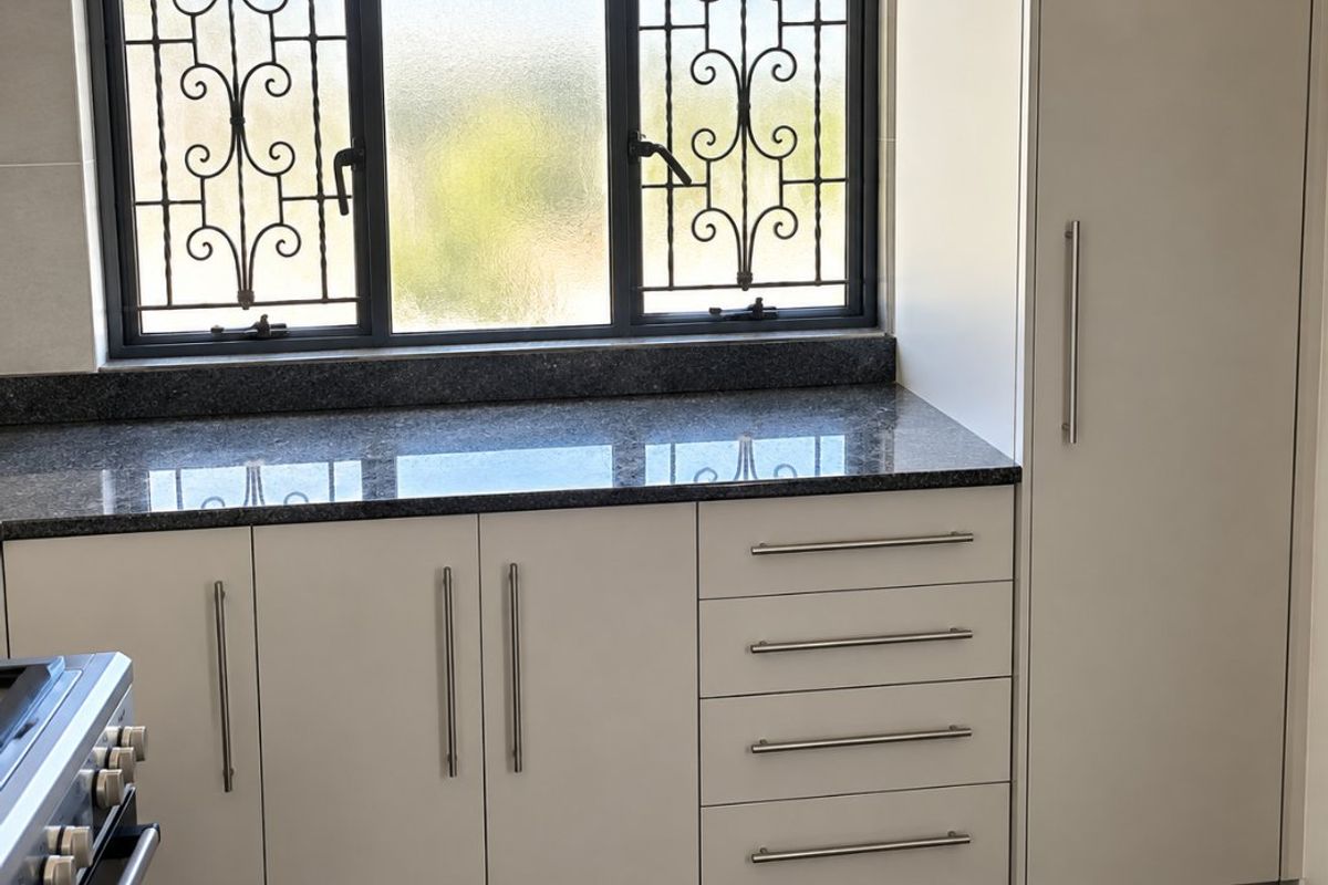 Modern kitchen featuring sleek cabinetry, granite countertops, and a window with security bars, offering a clean and functional workspace.