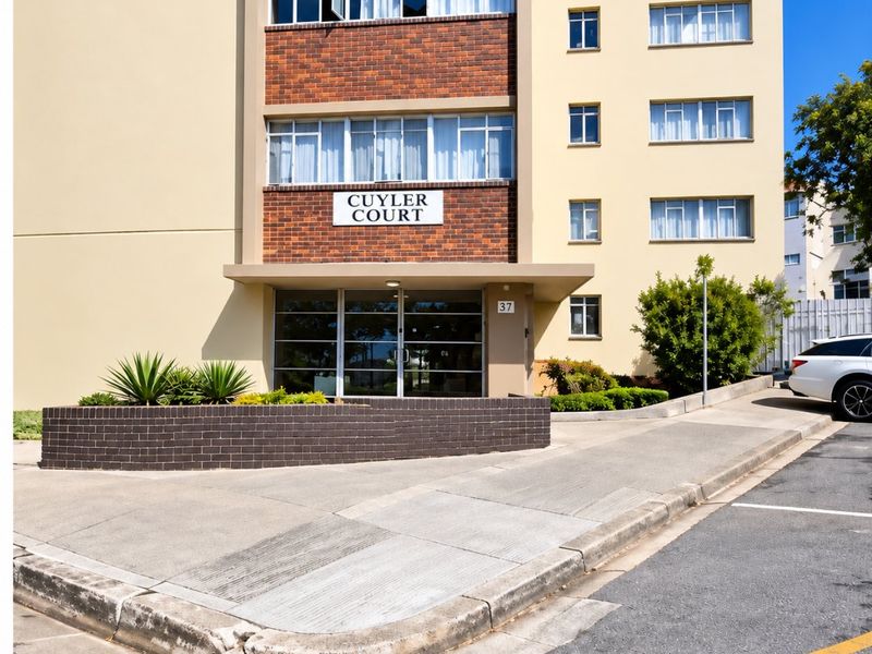 Front exterior view of Cuyler Court apartment building, featuring a brick facade, concrete driveway, and landscaped planter box at the entrance.