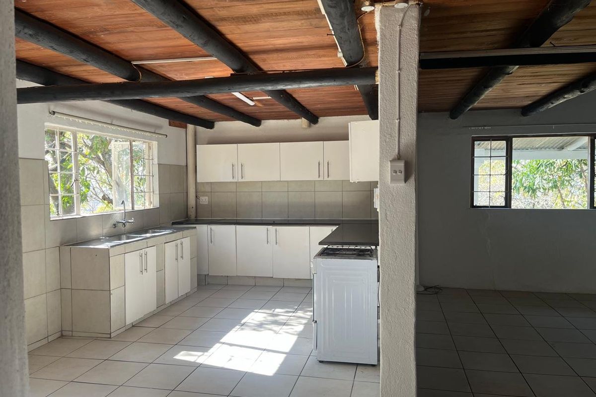 A functional kitchen featuring exposed timber ceiling beams, tiled flooring, ample built-in cabinetry, and a stainless steel sink, offering a rustic farm-style aesthetic.