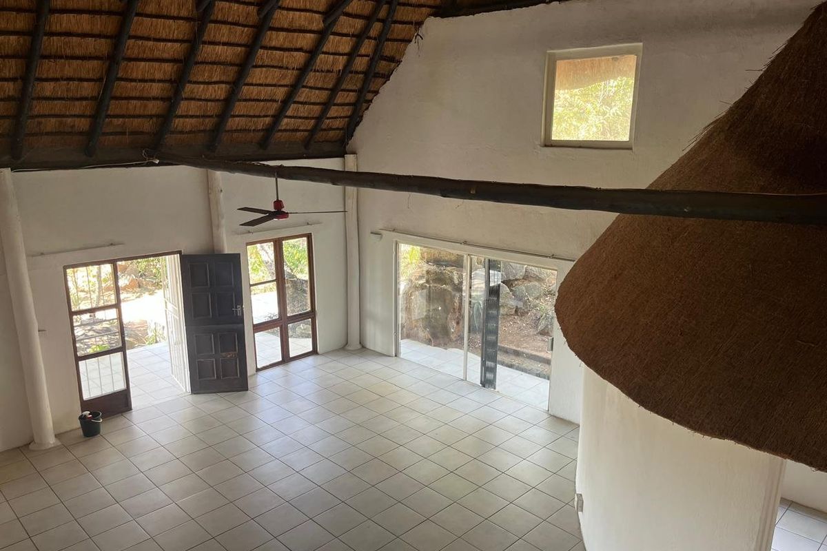 Spacious open-plan living area featuring a high thatched ceiling with exposed timber beams, tiled flooring, and large sliding doors leading to the exterior.