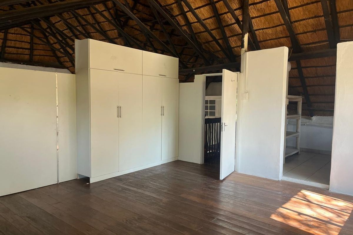 A spacious bedroom featuring exposed thatch roofing, timber flooring, and built-in cupboards, offering a rustic aesthetic with potential for modern updates.