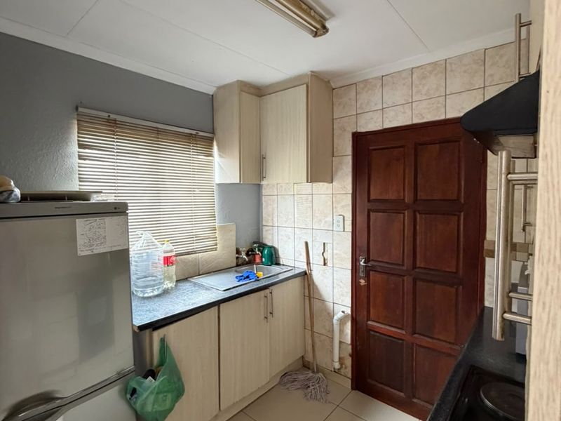 Compact kitchen featuring built-in cabinetry, tiled splashbacks, and integrated electric hob, offering a functional layout with potential for modern cosmetic updates.