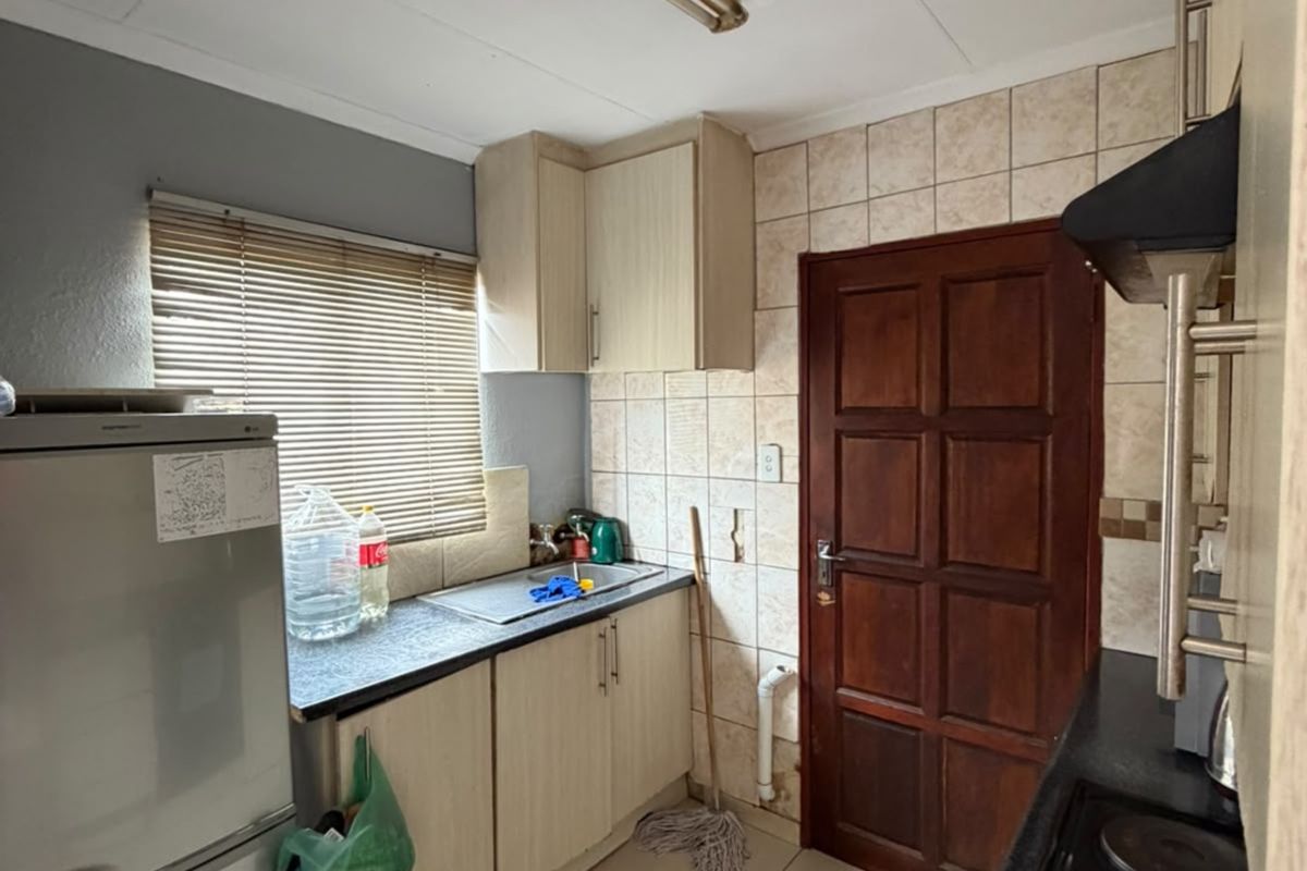 A functional kitchen featuring built-in cabinetry, laminate countertops, a stainless steel sink, and a tiled backsplash with an integrated electric hob and extractor fan.
