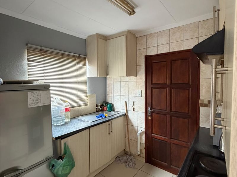 A functional kitchen featuring built-in cabinetry, laminate countertops, a stainless steel sink, and a tiled backsplash with an integrated electric hob and extractor fan.