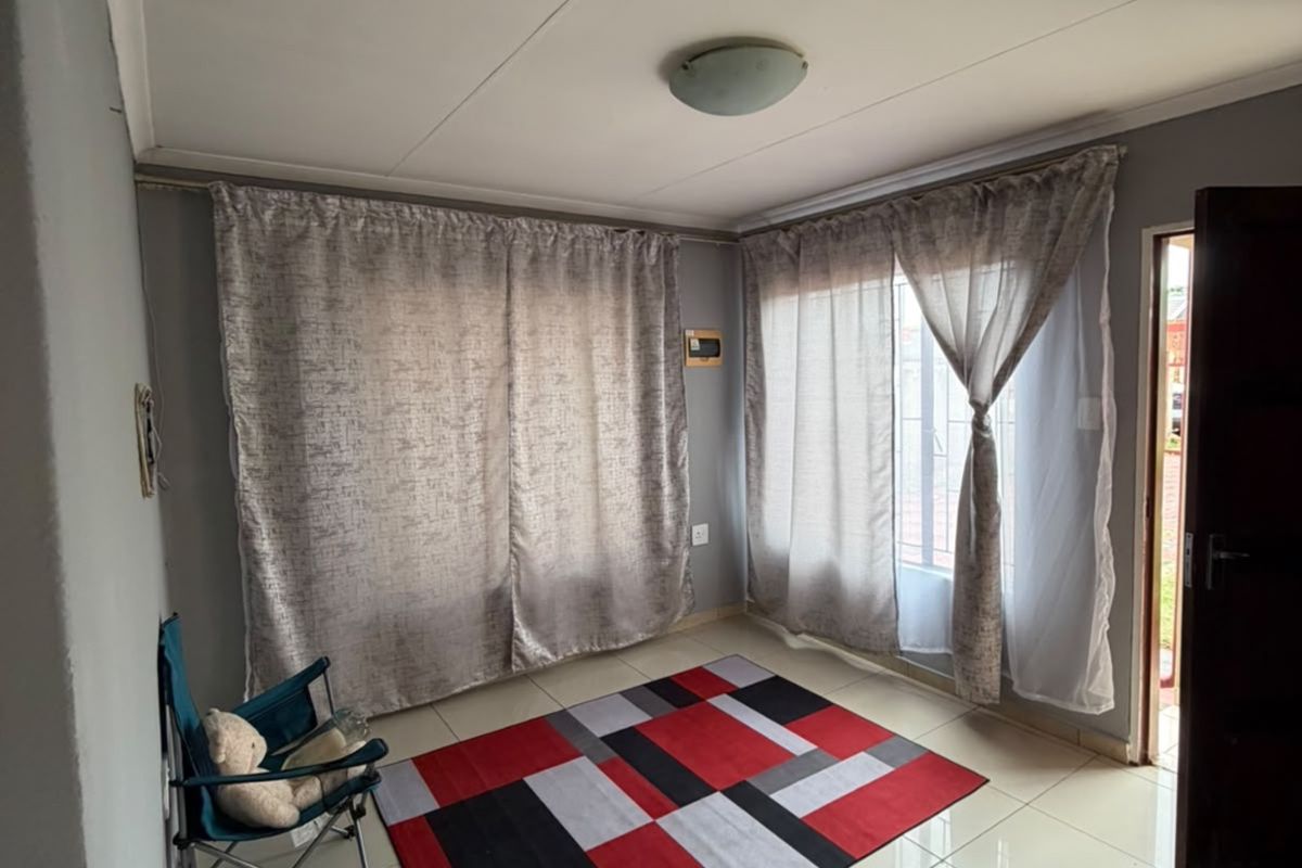 A bright, neutral living area featuring large windows with curtain rails and clean tiled flooring, offering a versatile space for interior design.