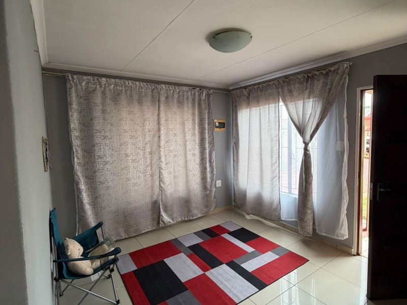 A bright, neutral living area featuring large windows with curtain rails and clean tiled flooring, offering a versatile space for interior design.