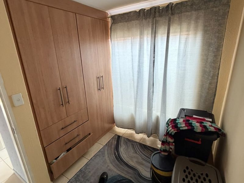 A bedroom featuring built-in wooden wardrobes, tiled flooring, and a window with curtains, offering functional storage space.