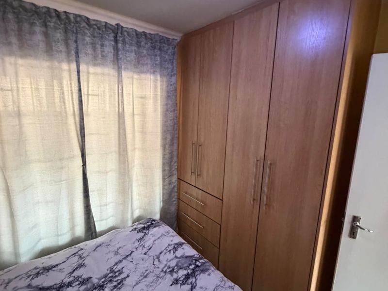 A bedroom featuring a large, light wood-toned built-in wardrobe with integrated drawers and a ceiling light fixture.