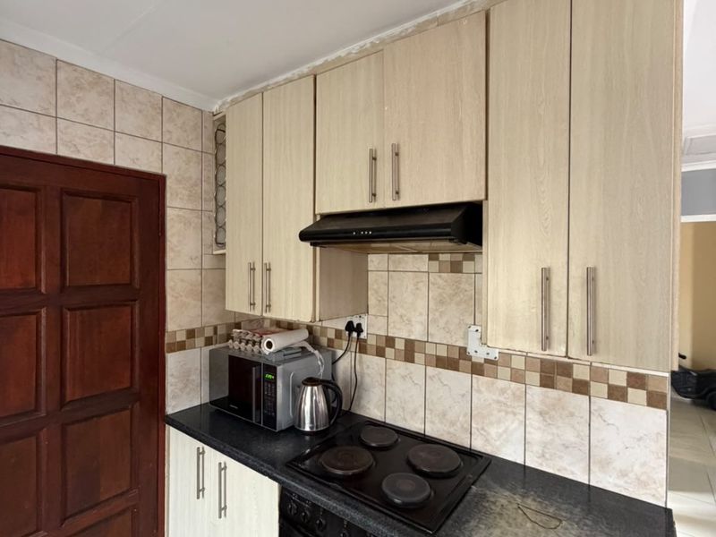 A functional kitchen featuring light wood-finish cabinetry, dark countertops, a built-in oven with electric hob, and a tiled backsplash.