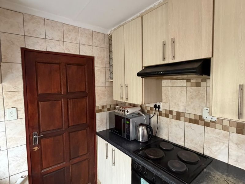 A compact kitchen featuring light wood-look cabinetry, a built-in electric oven and hob, tiled splashbacks, and tiled flooring.