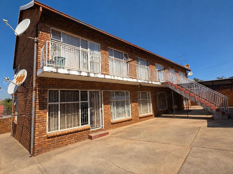 Exterior view of a two-story face brick apartment building featuring a metal staircase, balcony access, and paved courtyard area.