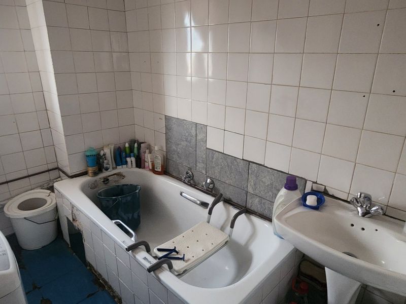A dated bathroom featuring a bathtub, pedestal basin, and toilet, requiring significant renovation and repair to the wall and floor tiling.