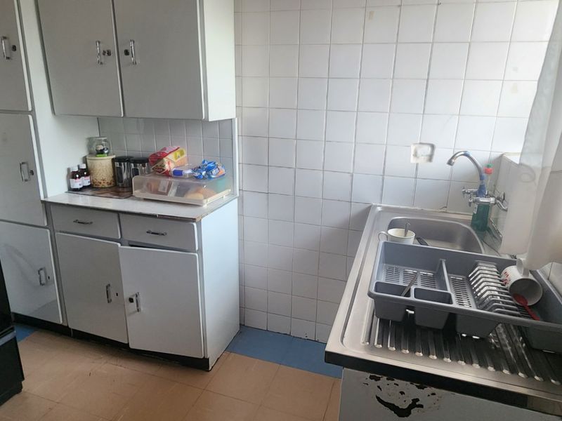 A dated kitchen featuring original cabinetry, tiled splashbacks, and a stainless steel sink, offering significant potential for modernization and renovation.