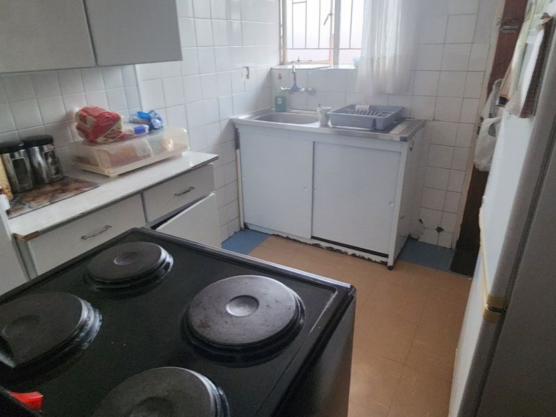 A functional kitchen featuring built-in cabinetry, a stainless steel sink, and an electric stove, with tiled walls and flooring throughout.
