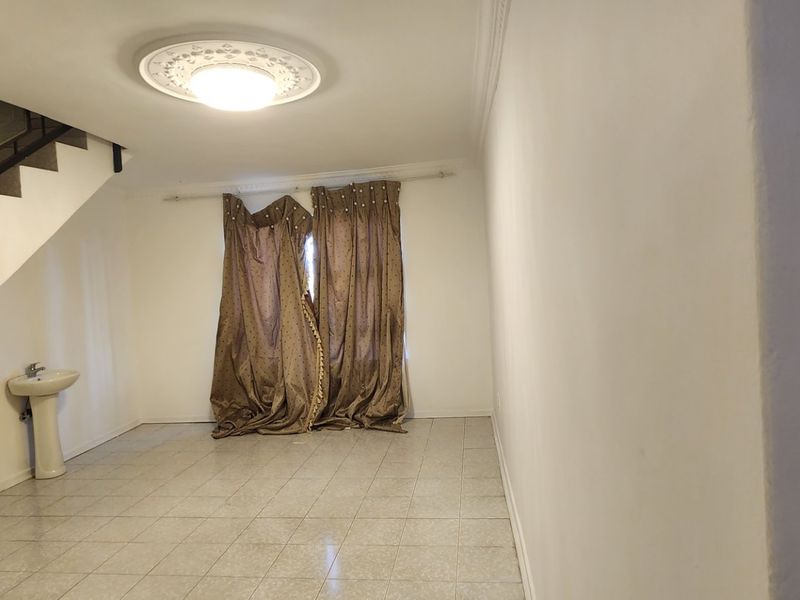 An open-plan living area featuring tiled flooring, a decorative ceiling rose, and a convenient pedestal basin located beneath the staircase.