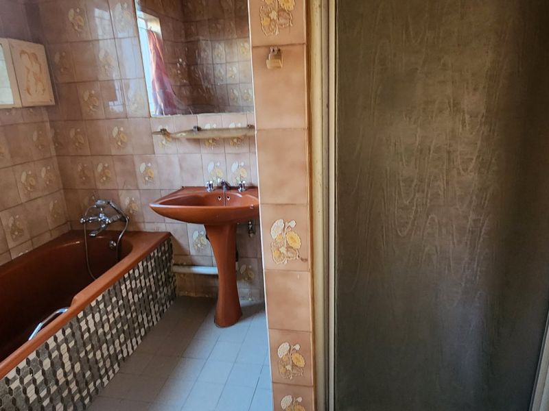 A dated bathroom featuring a pedestal basin, built-in bathtub, and separate shower enclosure with original wall tiling.