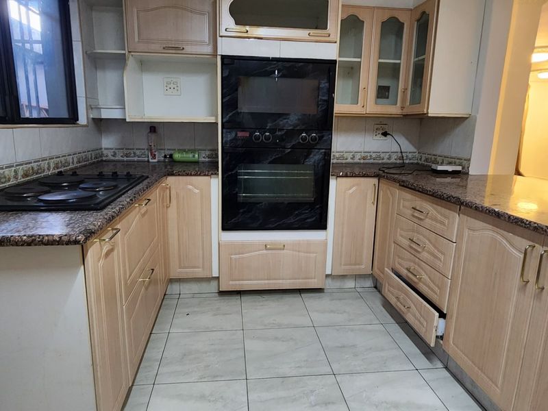 A functional kitchen featuring light wood cabinetry, granite countertops, a built-in oven, and an electric hob, with an open-plan layout connecting to the living area.