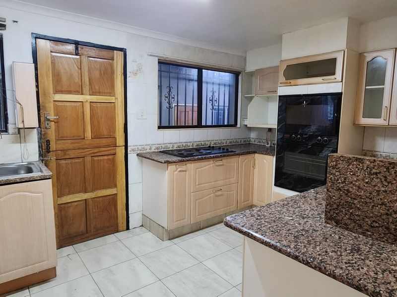 A functional kitchen featuring granite countertops, built-in oven, hob, and ample cabinetry, offering a solid foundation for a modern cosmetic update.