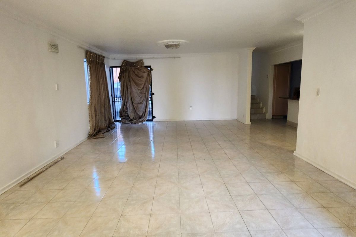 A spacious, empty living area featuring neutral ceramic floor tiles, a decorative ceiling rose, and access to an exterior security gate.