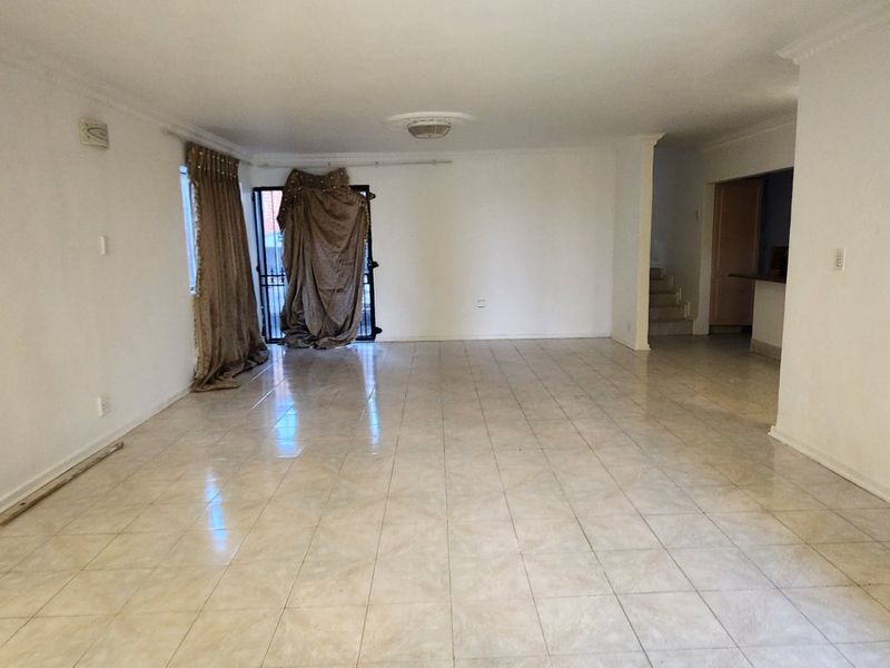 A spacious, empty living area featuring neutral ceramic floor tiles, a decorative ceiling rose, and access to an exterior security gate.