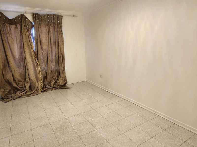 An empty living room featuring tiled flooring, crown molding, and a window with a curtain rod, requiring minor cosmetic updates.