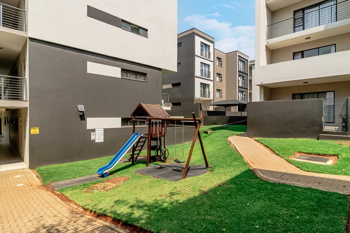 A communal outdoor area between townhouse blocks featuring paved walkways, landscaped lawn, and residential balconies.