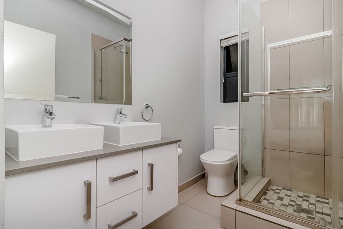 Modern bathroom featuring a double vanity with white cabinetry, a glass-enclosed shower with tiled flooring, and neutral wall finishes.